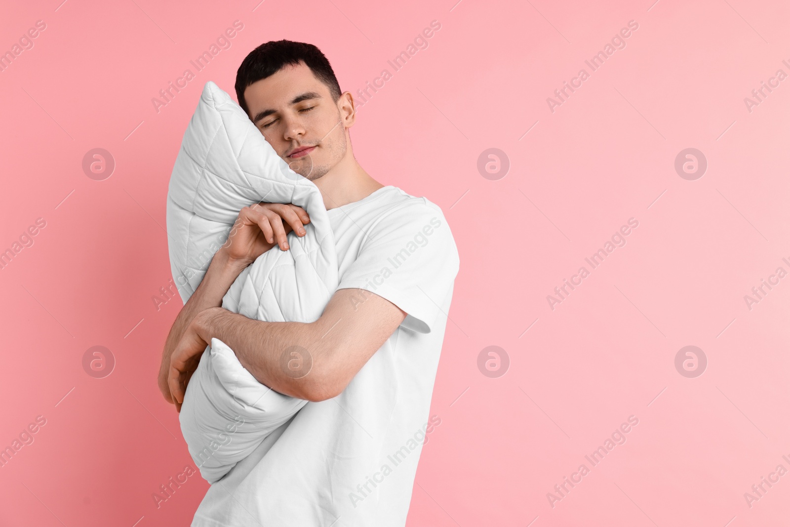 Photo of Man in pyjama holding pillow and sleeping on pink background, space for text