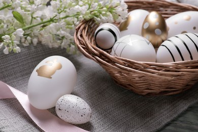 Photo of Many painted Easter eggs, branch with lilac flowers and ribbon on table