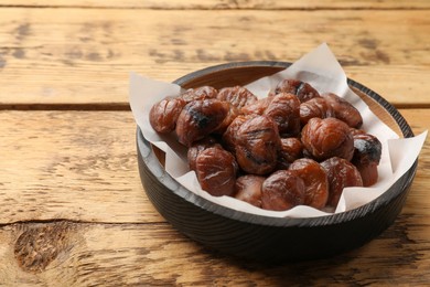 Photo of Roasted edible sweet chestnuts in bowl on wooden table, space for text