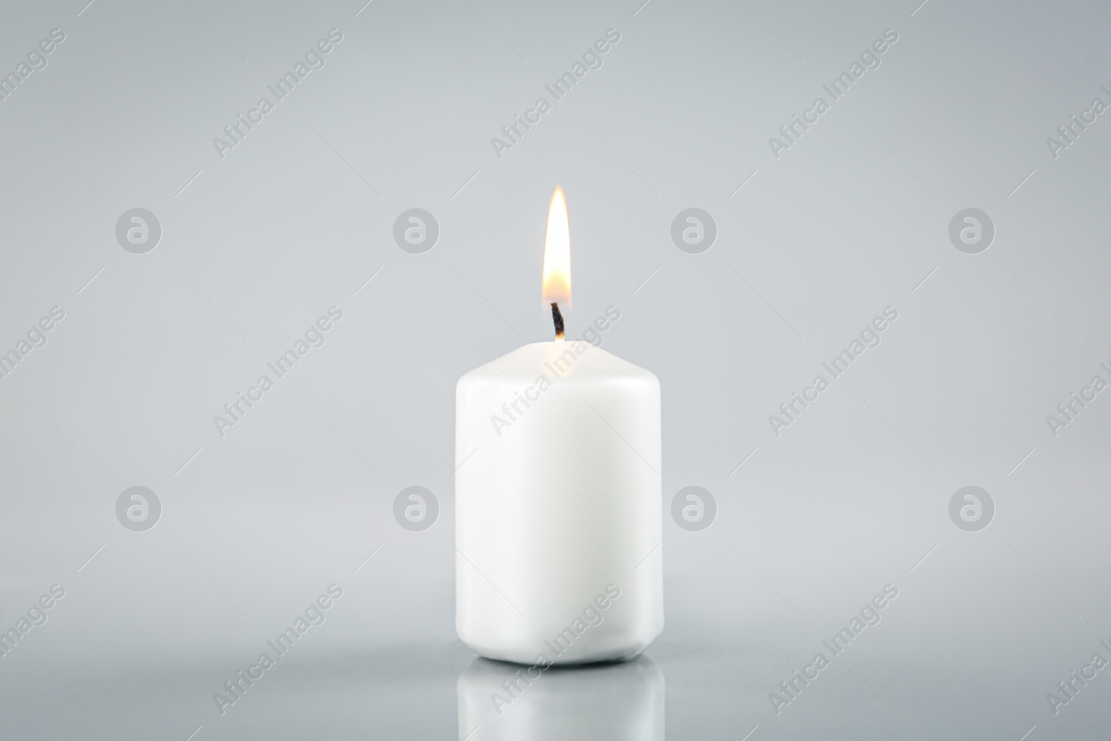 Photo of Burning white candle on light grey background