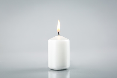 Photo of Burning white candle on light grey background