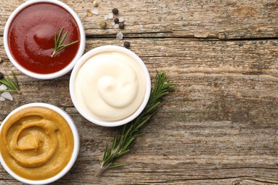 Different tasty sauces in bowls, rosemary and spices on wooden table, flat lay. Space for text