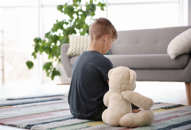 Lonely little boy with teddy bear sitting on floor at home. Autism concept