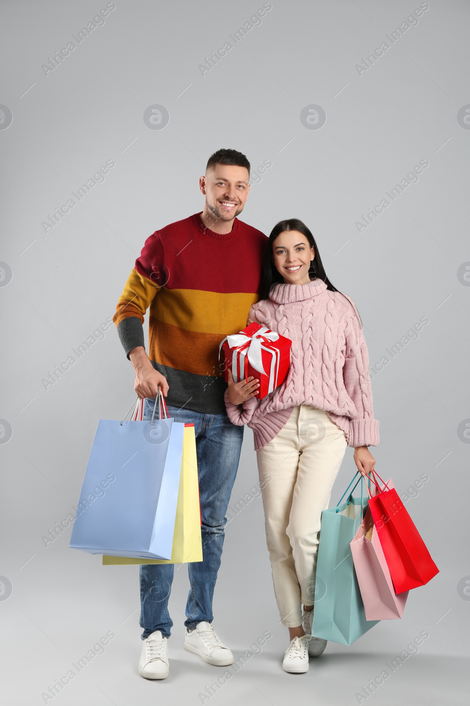 Photo of Happy couple with paper bags and gift on grey background. Christmas shopping