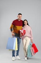 Photo of Happy couple with paper bags and gift on grey background. Christmas shopping
