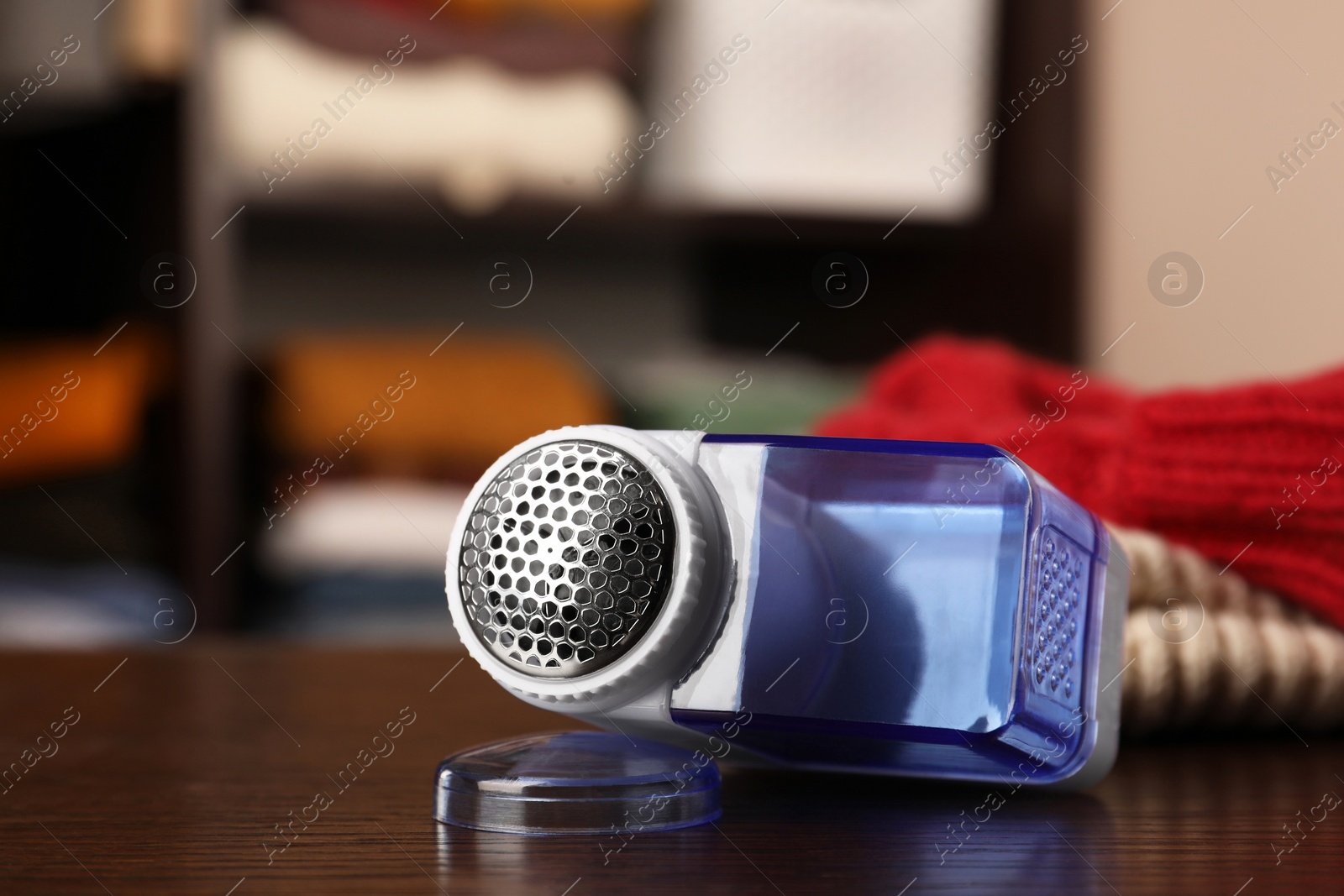 Photo of Modern fabric shaver and knitted clothes on wooden table indoors, closeup. Space for text