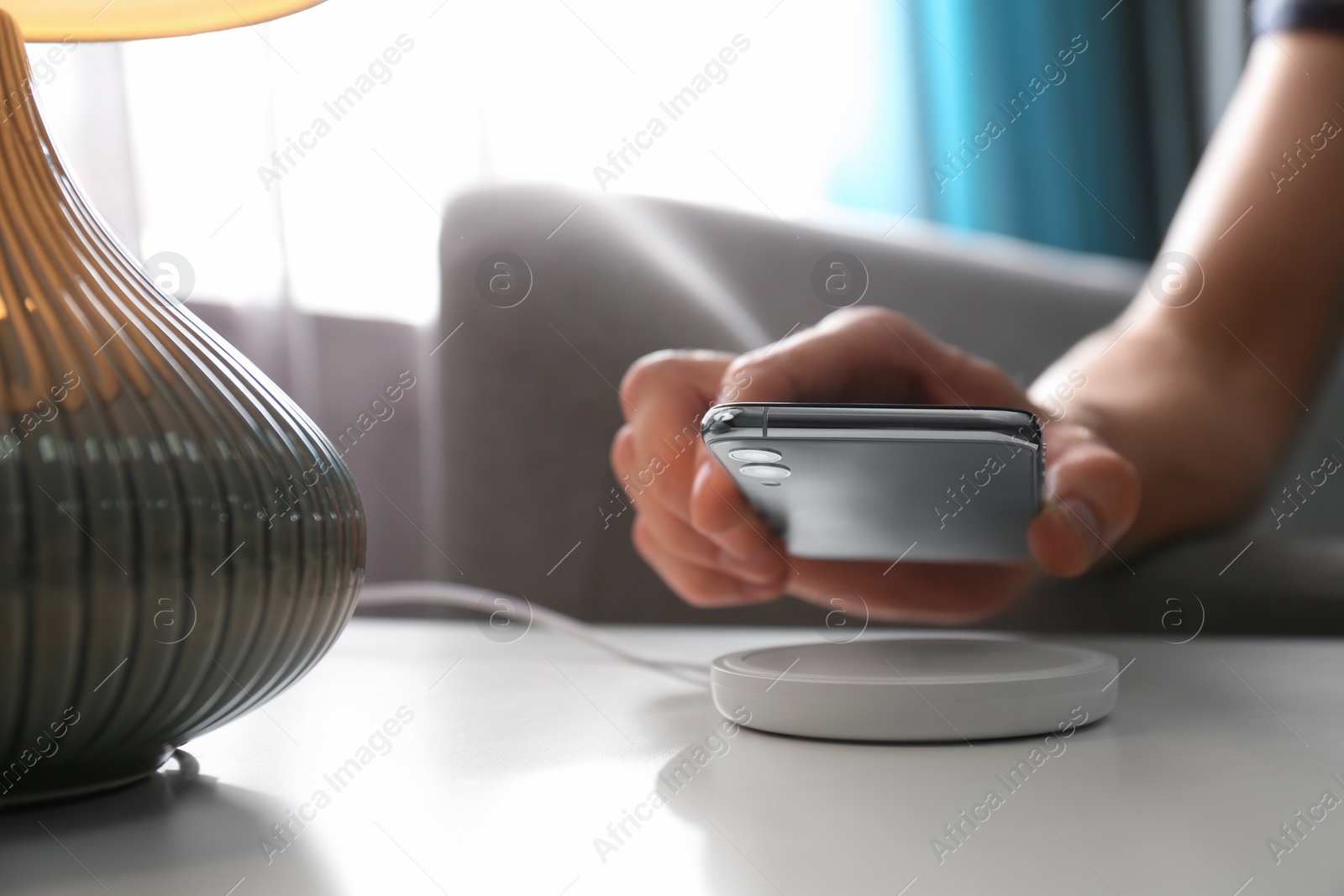 Photo of Man putting smartphone on wireless charger in room, closeup