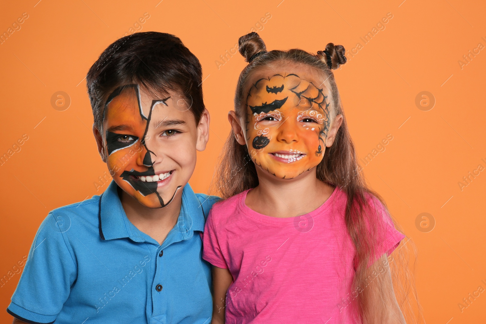 Photo of Cute little children with face painting on orange background