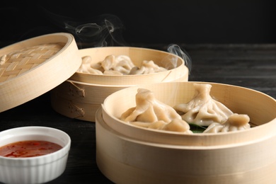 Bamboo steamers with tasty baozi dumplings and bowl of sauce on table