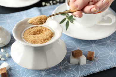 Woman taking spoon of brown sugar from bowl at table, closeup