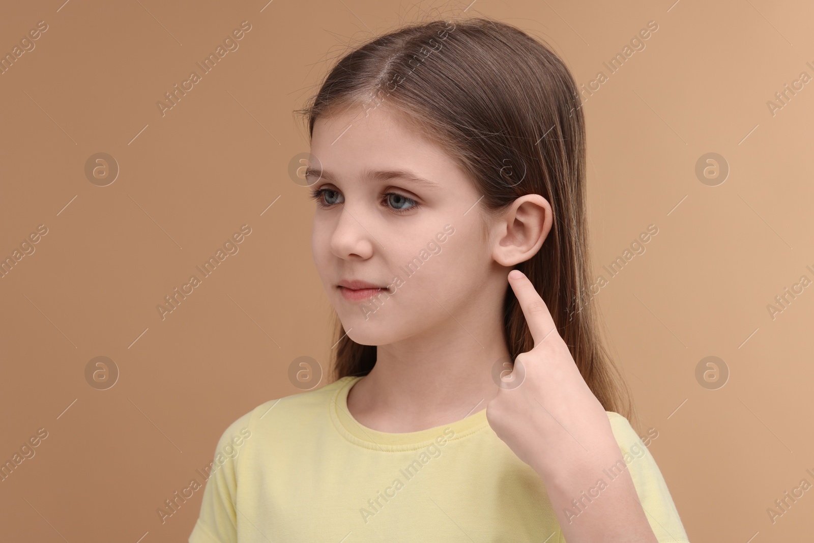 Photo of Hearing problem. Little girl pointing at ear on pale brown background