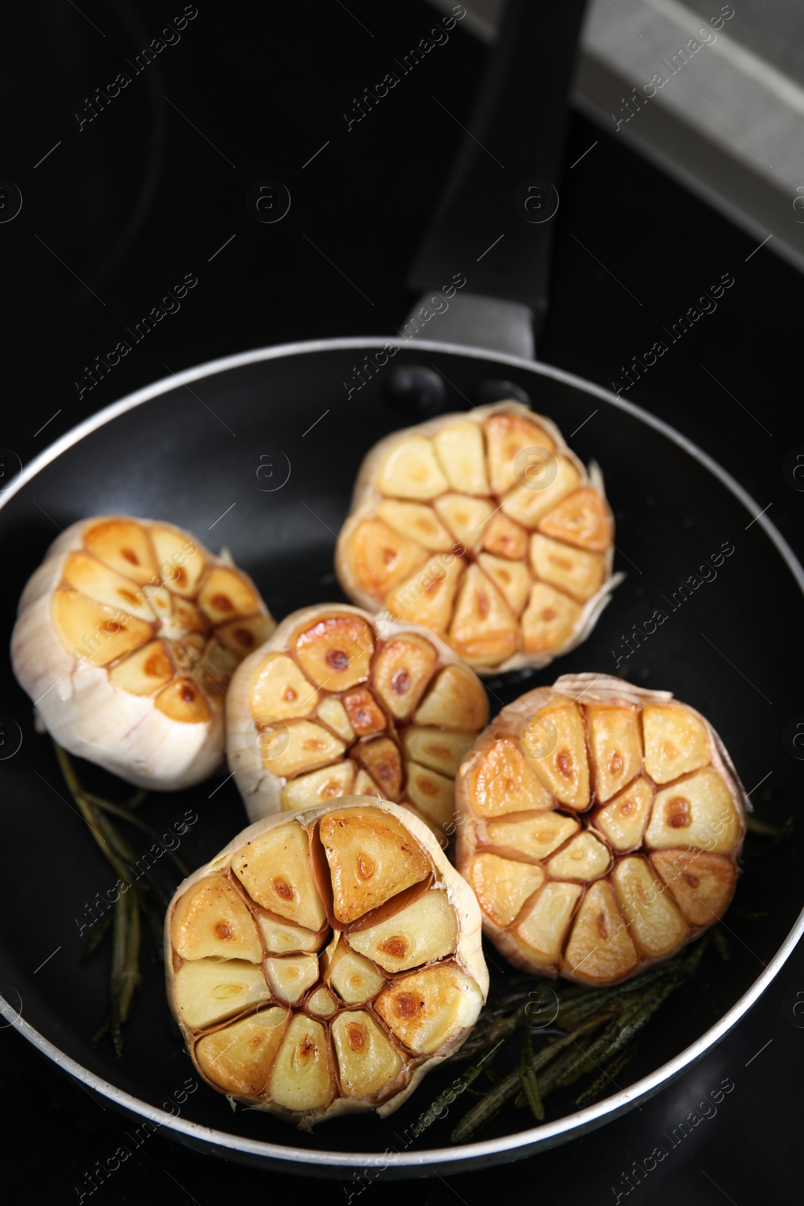 Photo of Frying pan with fried garlic and rosemary on stove, closeup