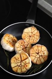 Photo of Frying pan with fried garlic and rosemary on stove, closeup