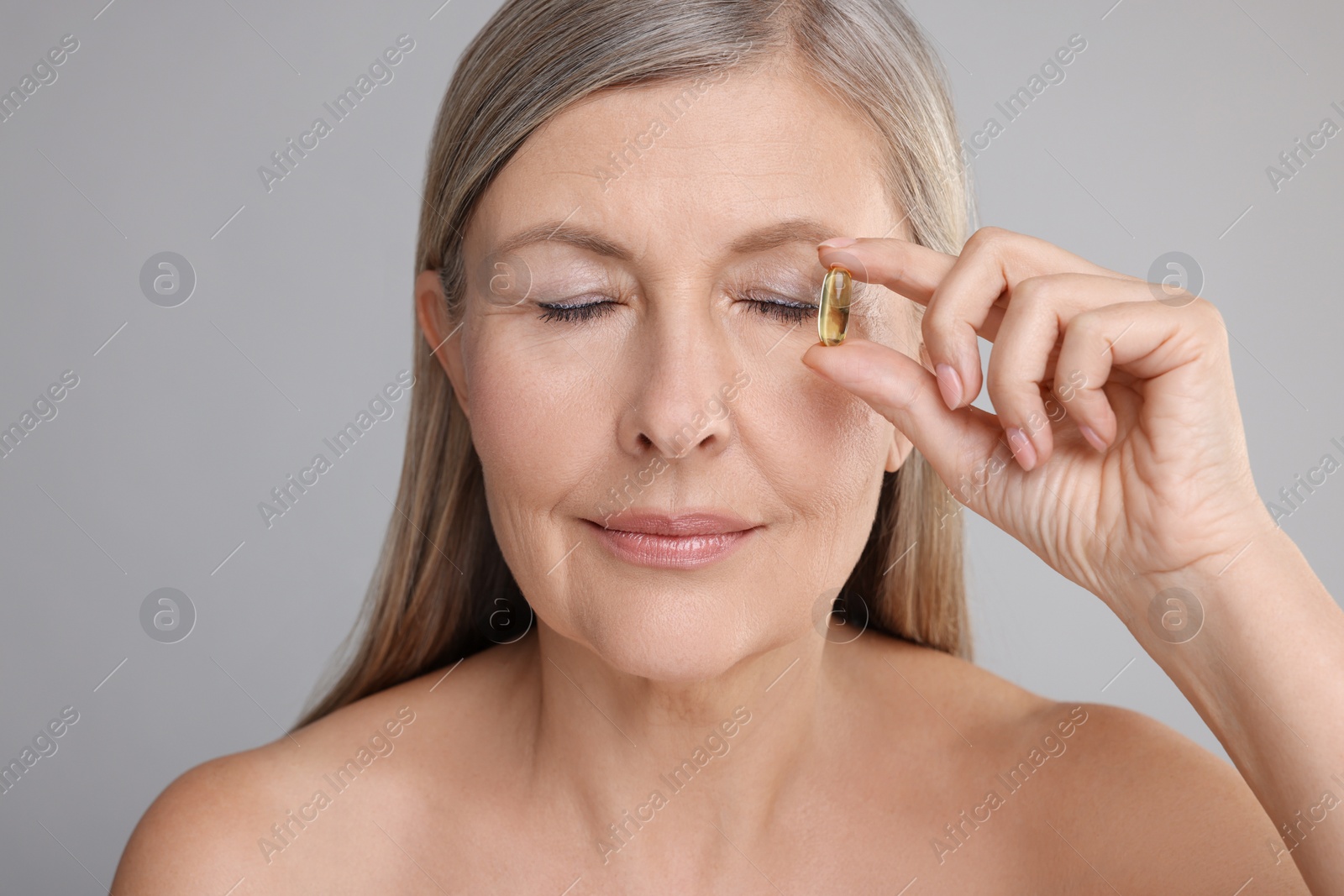 Photo of Beautiful woman with vitamin capsule on grey background