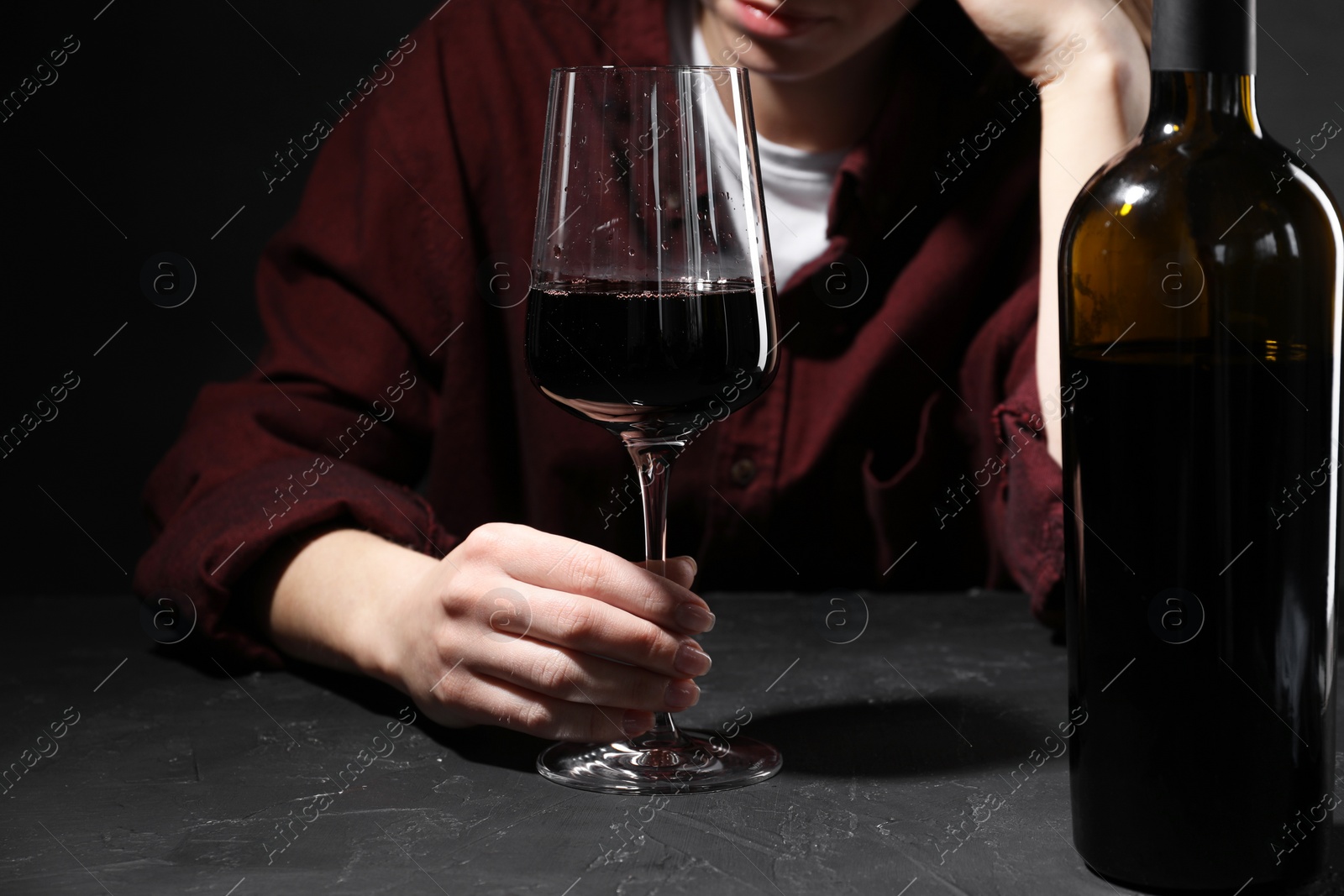 Photo of Alcohol addiction. Woman with red wine at dark textured table, selective focus