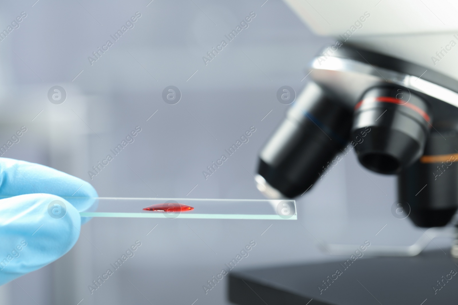 Photo of Scientist holding microscope slide with sample of red liquid in laboratory, closeup