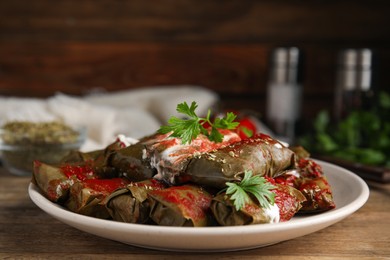 Photo of Delicious stuffed grape leaves with sour cream and tomato sauce on wooden table
