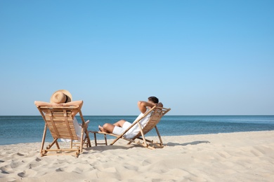 Photo of Young couple relaxing in deck chairs on beach