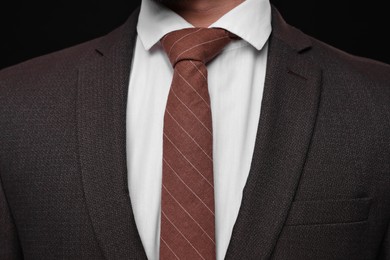 Businessman in suit and necktie on black background, closeup