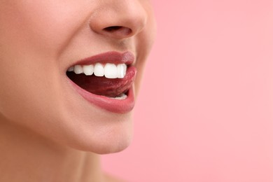 Woman with beautiful lips licking her teeth on pink background, closeup. Space for text