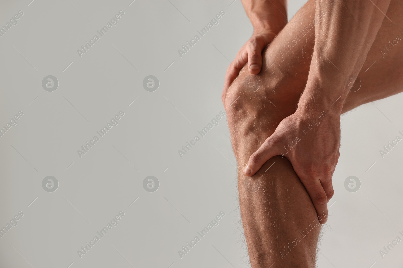 Photo of Man touching his muscular legs on light grey background, closeup. Space for text