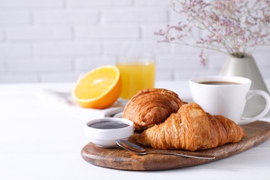 Photo of Tasty breakfast. Cup of coffee, jam and croissants on white wooden table, space for text