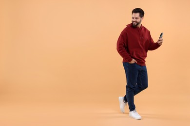 Happy young man using smartphone on beige background, space for text