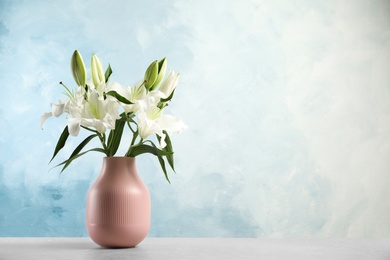 Vase of beautiful lilies on table against blue background, space for text