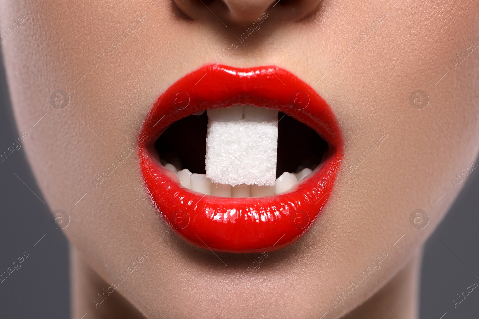 Photo of Closeup view of young with beautiful lips eating sugar cube on grey background