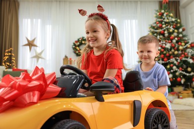 Photo of Cute little boy pushing toy car with his sister in room decorated for Christmas