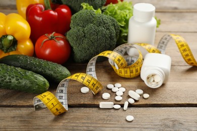 Photo of Weight loss pills, different vegetables and measuring tape on wooden table