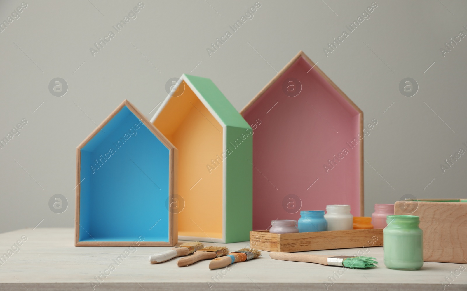 Photo of House shaped shelves, jars of paints and brushes on white table. Interior elements