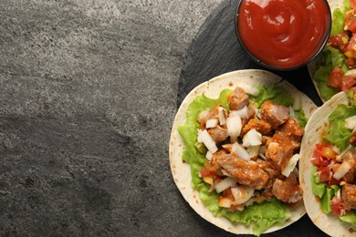 Photo of Delicious tacos with vegetables, meat and ketchup on grey textured table, top view. Space for text