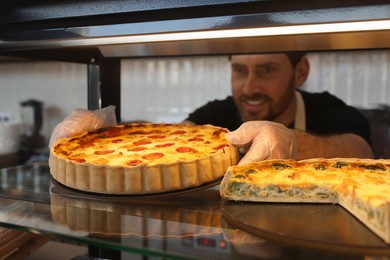 Photo of Happy seller taking tasty quiche from showcase in bakery, selective focus