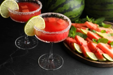 Cocktail glasses of delicious fresh watermelon juice with lime and sugar rim on black table