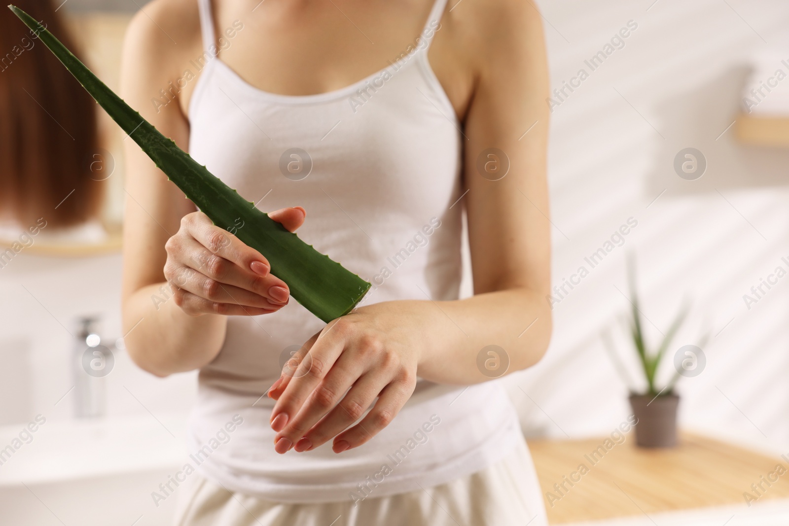 Photo of Young woman applying aloe gel from leaf onto her hand in bathroom, closeup