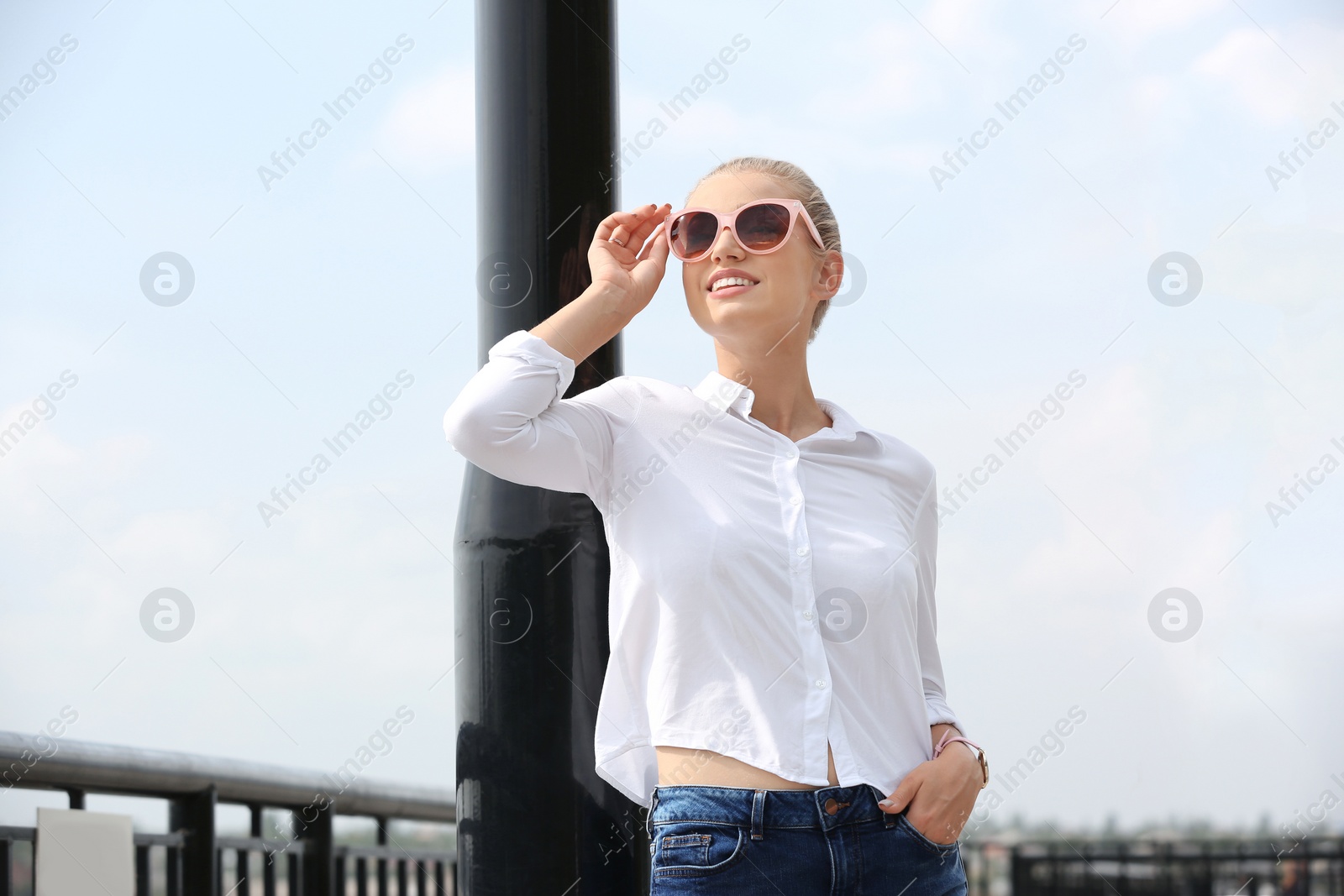 Photo of Beautiful young woman with sunglasses standing at pier. Joy in moment