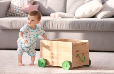 Photo of Cute baby holding on to wooden cart in living room. Learning to walk