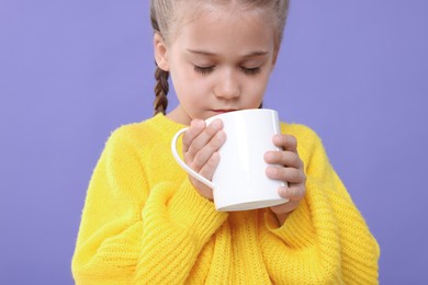 Photo of Cute girl drinking beverage from white ceramic mug on violet background