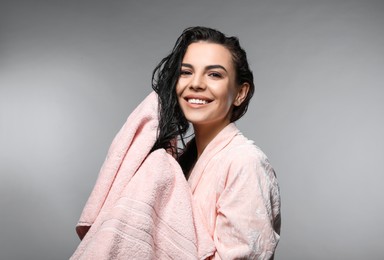 Photo of Happy young woman drying hair with towel after washing on light grey background