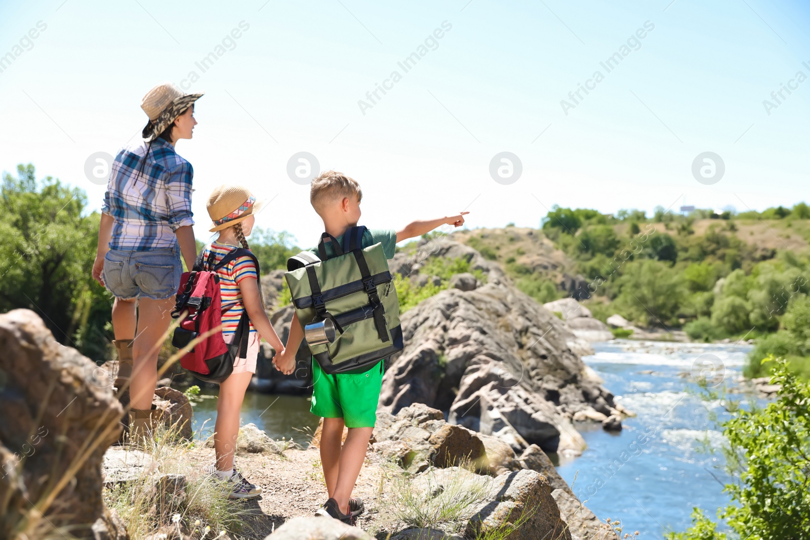 Photo of Young woman with children on rock near river. Summer camp