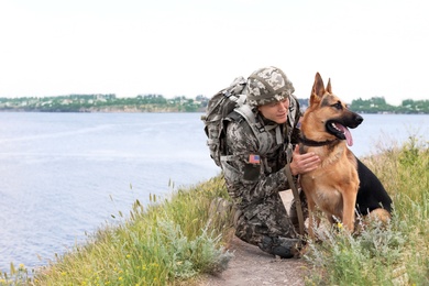 Photo of Man in military uniform with German shepherd dog near river
