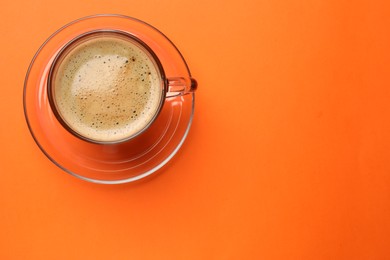 Photo of Fresh coffee in cup on orange background, top view. Space for text