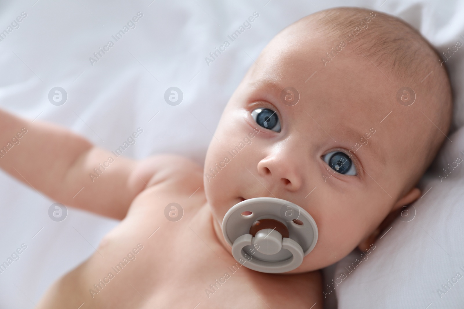 Photo of Cute little baby with pacifier lying on bed, closeup