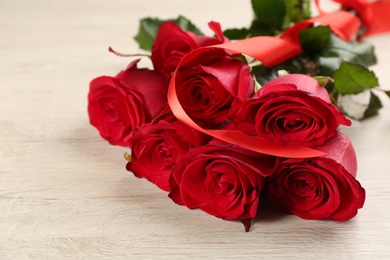 Photo of Beautiful red roses with ribbon on white wooden background, closeup. Valentine's Day celebration