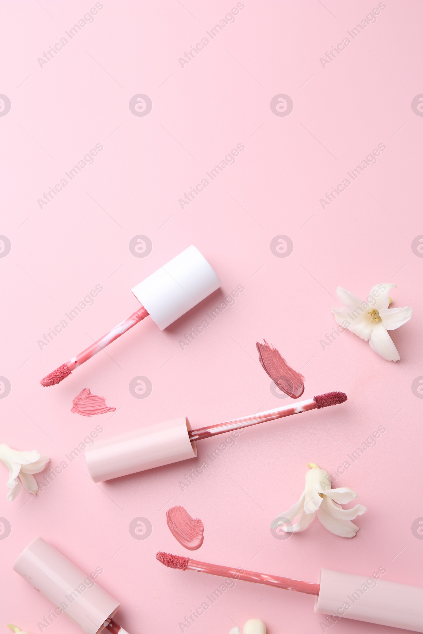 Photo of Different lip glosses, applicators and flowers on pink background, flat lay. Space for text