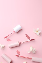 Photo of Different lip glosses, applicators and flowers on pink background, flat lay. Space for text