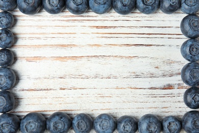 Photo of Frame made with fresh blueberries on white wooden table, top view. Space for text