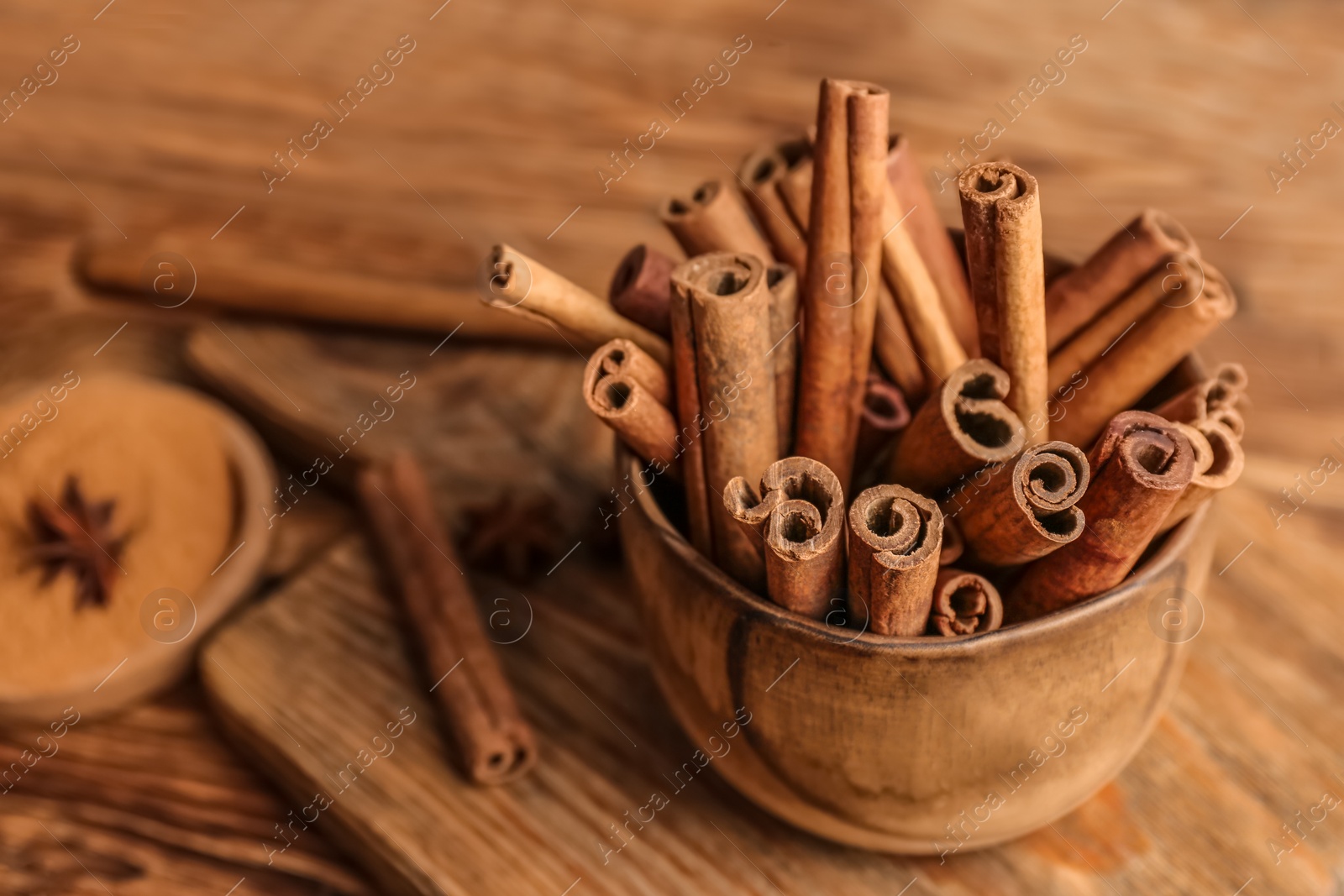 Photo of Bowl with aromatic cinnamon sticks on wooden background