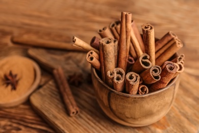 Photo of Bowl with aromatic cinnamon sticks on wooden background